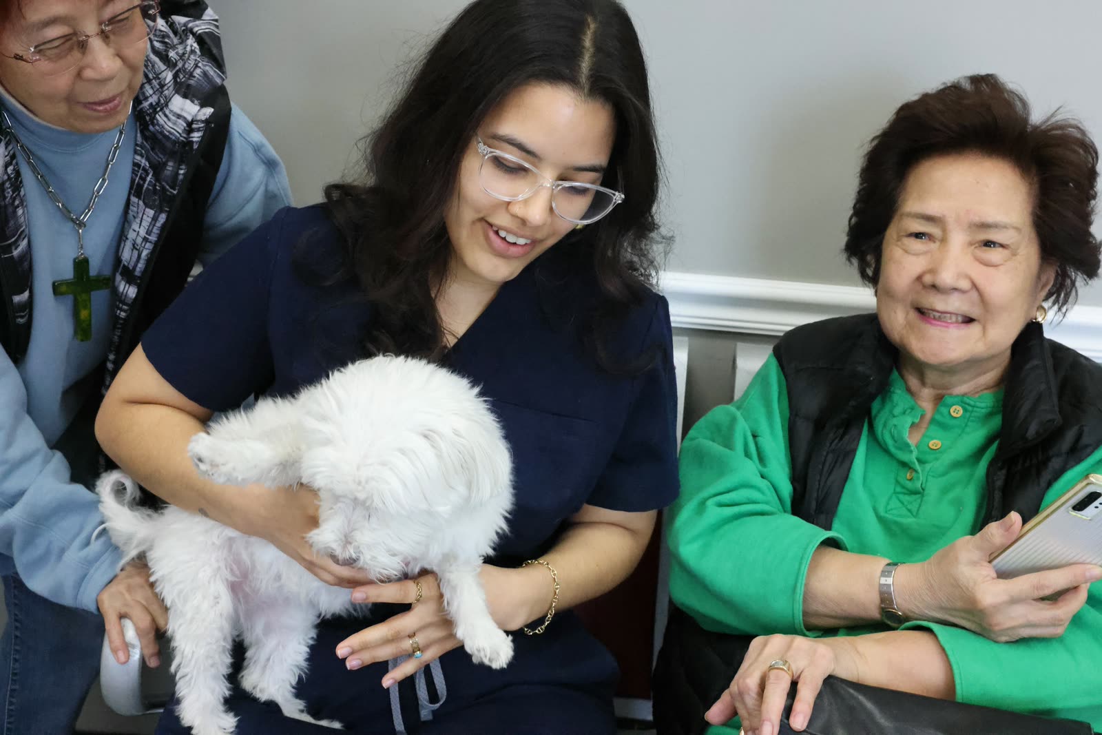 Clifton Ave Animal Hospital team member Amber holding a client's small white dog in the lobby, with two smiling clients seated beside her